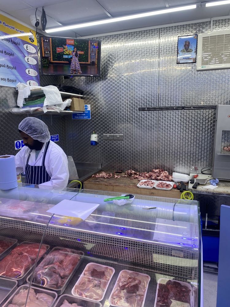 A butcher in a white coat working behind the chilled display counter, trays of red meat in the case.