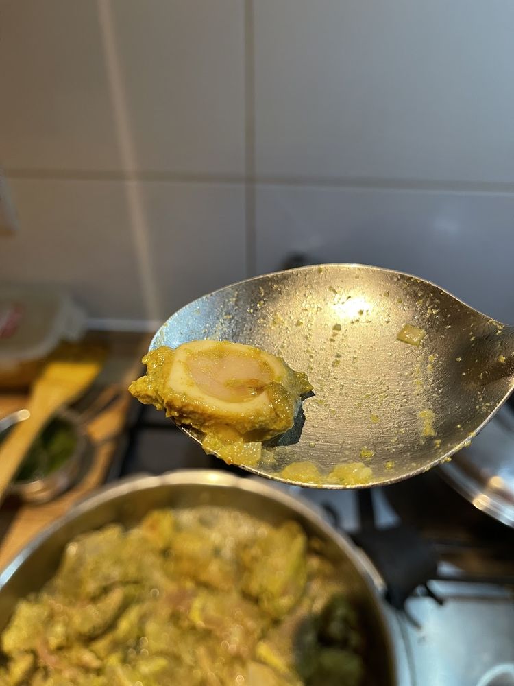 A ladle lifting a piece of meat from a pot of yellow curry on the stove.